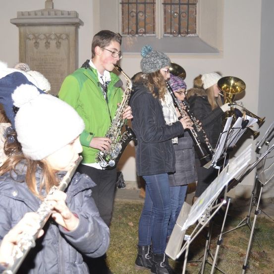 Eine Gruppe junger Musiker tritt bei Nacht im Freien auf, einige spielen Saxophon, andere Klarinette und einige spielen Trompete.