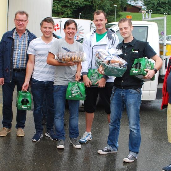 Mehrere Männer stehen draußen in einer Gruppe und halten Tüten. Ein Mann hält ein Brot. Sie sind draußen in der Nähe eines weißen Lieferwagens.