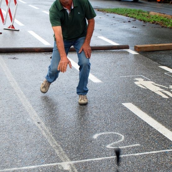 Ein Mann steht auf einer nassen Straße mit der Nummer '2' darauf, mit dem Rücken zur Kamera.