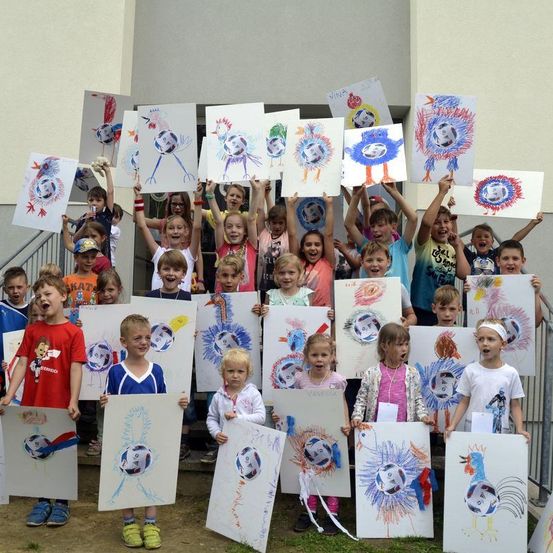 Eine Gruppe von Kindern steht zusammen und hält jedes ein Kunstwerk mit einem Fußballdesign hoch. Sie tragen alle verschiedenfarbige Kleidung und scheinen für ein Foto zu posieren.