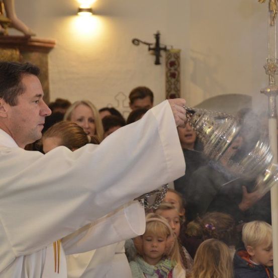 Ein Priester hält einen silbernen Kelch, aus dem Rauch aufsteigt, während er eine Zeremonie in einer Kirche mit einem Publikum durchführt.