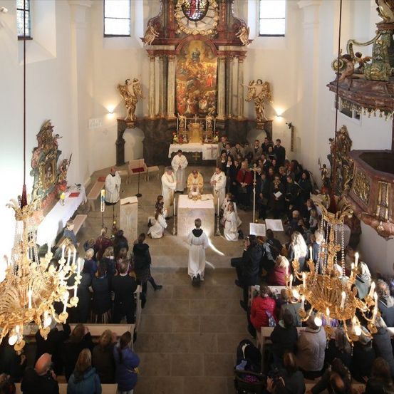 Ein Priester leitet eine religiöse Zeremonie in einer dekorierten Kirche, die von einer großen Menschenmenge beobachtet wird.