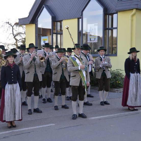 Eine Brass-Band in traditioneller Kleidung steht vor einem Gebäude. Eine Frau steht in der Nähe in traditioneller Kleidung.