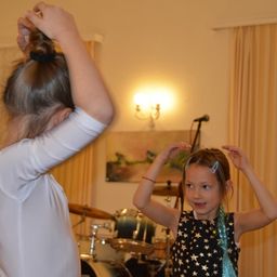 Zwei junge Mädchen tanzen in einem Raum mit Musikinstrumenten. Das Mädchen rechts trägt ein sternenförmiges Kleid.