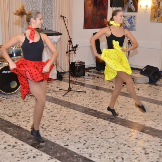 Zwei Frauen tanzen auf einer Bühne mit Musikinstrumenten und Lautsprechern im Hintergrund.