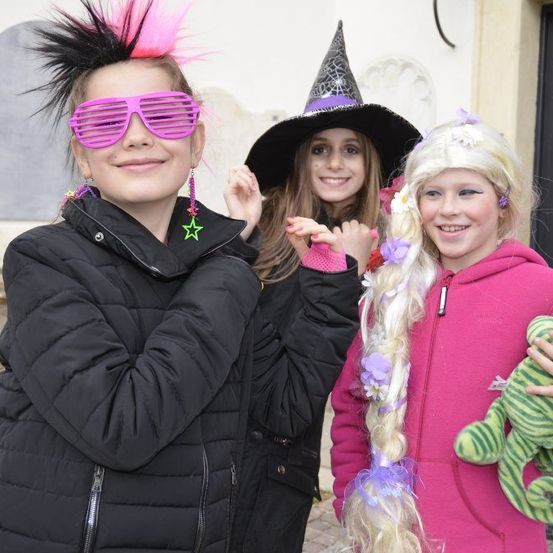 Drei junge Mädchen, die für eine Halloween-Feier verkleidet sind. Eine trägt einen Hexenhut, eine andere hat rosa Sonnenbrille und die dritte hält ein grünes Kuscheltier.