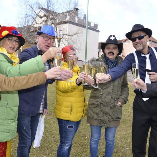 Eine Gruppe von Menschen in Kostümen, die Champagnergläser halten, stehen draußen auf einem Rasenfeld.