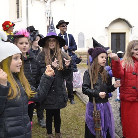 Eine Gruppe von Kindern, die als Hexen und andere Charaktere verkleidet sind, stehen vor einer Kirche. Einige tragen Hüte und eine hält einen Besen. Ein Mann steht in der Nähe.