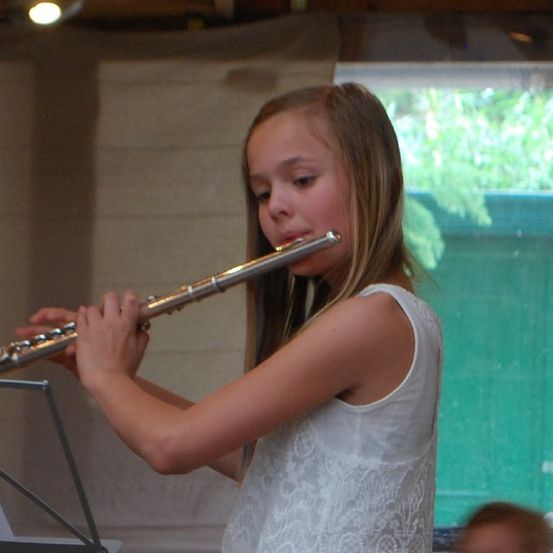 Ein Mädchen spielt Flöte in einem Raum mit einem Fenster im Hintergrund.