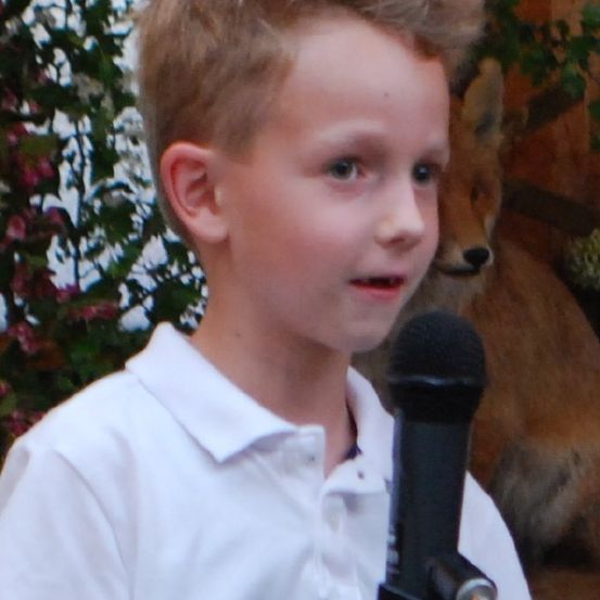 Ein Junge spricht in ein Mikrofon, mit einem Fuchs im Hintergrund.