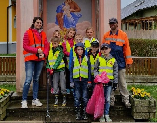 Eine Gruppe von Kindern und Erwachsenen in Warnwesten posiert für ein Foto vor einem Gebäude mit einem religiösen Wandbild.