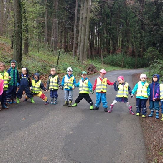 Eine Gruppe von Kindern in gelben Westen und Stiefeln posiert für ein Foto auf einer Straße im Wald.