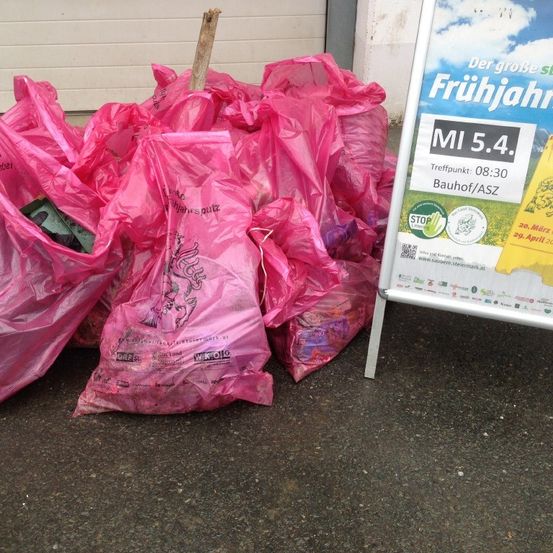 Ein Haufen rosa Plastiktüten auf dem Boden mit einem Plakat für eine Veranstaltung.