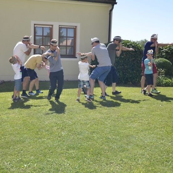 Mehrere Menschen in Hüten üben Kampfkunst auf einem Rasen vor einem Haus. Ein Kind liegt auf dem Gras.