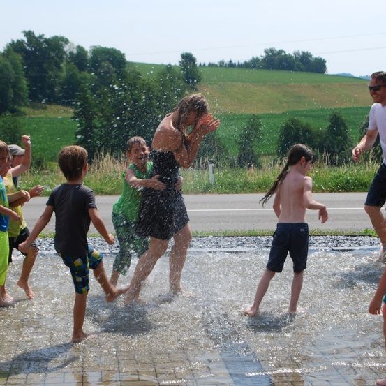 Kinder spielen in einem Brunnen, eine Mädchen lacht und hält einen Jungen, an einem sonnigen Tag.