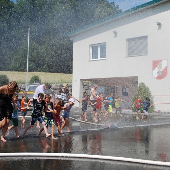 Eine Gruppe von Kindern und Erwachsenen spielt in einem Springbrunnen vor einem Gebäude.