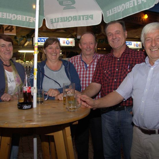 Fünf Personen posieren für ein Foto an einem Restauranttisch mit Getränken und einem Schirm mit dem Wort 'Biergarten'.