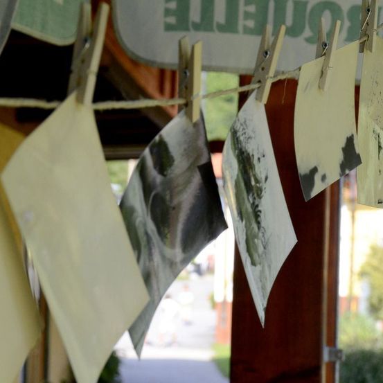 Mehrere Fotos sind an einem Seil unter einem Schild mit dem Wort 'Photographie' befestigt. Die Fotos sind größtenteils schwarz-weiß.