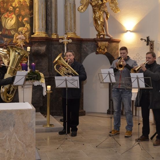 Vier Musiker spielen Blechblasinstrumente in einer Kirche mit Kerzen und religiösen Kunstwerken.
