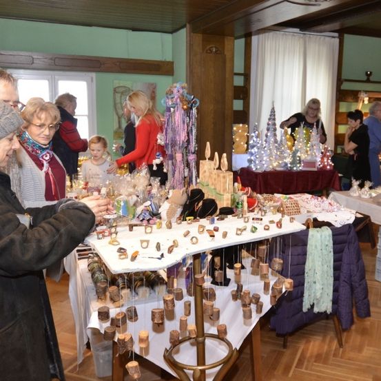 Ein Raum gefüllt mit verschiedenen Artikeln zum Verkauf. Die Leute stöbern über die Artikel auf dem Tisch. Es gibt auch Weihnachtsbäume und Lichter auf dem Tisch.