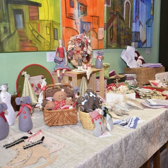 Ein Tisch mit verschiedenen Stofftieren und Stoffen, einem Korb mit Spielzeug und einem Regal mit Gemälden an der Wand.