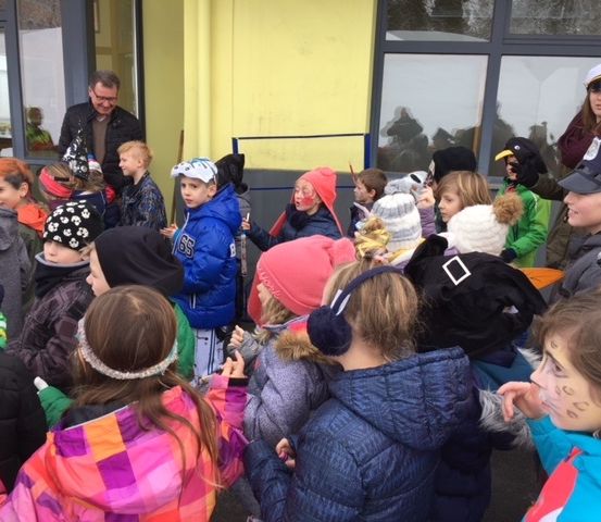Eine Gruppe von Kindern und Erwachsenen versammelt sich vor einem Gebäude. Die Kinder tragen verschiedene Gesichtsbemalungen und Mützen. Ein Erwachsener in einer Polizeimütze schaut sie an.