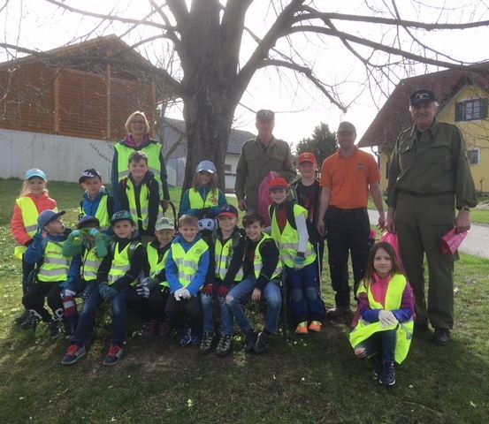 Gruppenfoto von Kindern, Erwachsenen und einem großen Baum mit zwei Männern in Uniform, alle lächeln für die Kamera in einem Park.