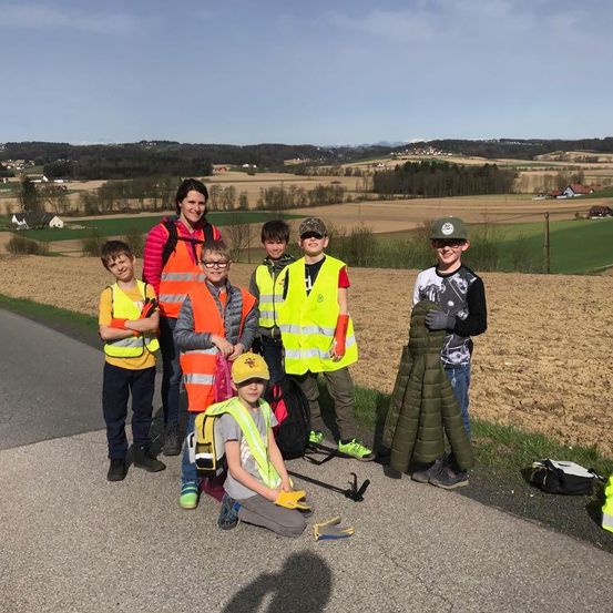 Eine Gruppe von Kindern in Sicherheitswesten posiert für ein Foto am Straßenrand mit einer ländlichen Landschaft im Hintergrund.
