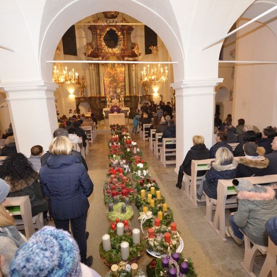 Eine Gemeinde in einer Kirche, mit einem Altar am Ende, geschmückt mit Blumen und Kerzen. Der Priester steht vor dem Altar, und die Gemeinde sitzt auf beiden Seiten des Mittelgangs.