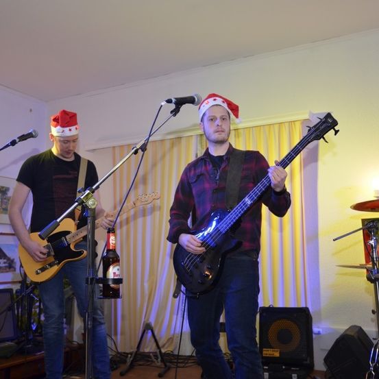 Zwei Männer spielen auf der Bühne und tragen Weihnachtsmützen. Einer spielt Gitarre, der andere Bassgitarre. Dahinter steht ein Schlagzeug.