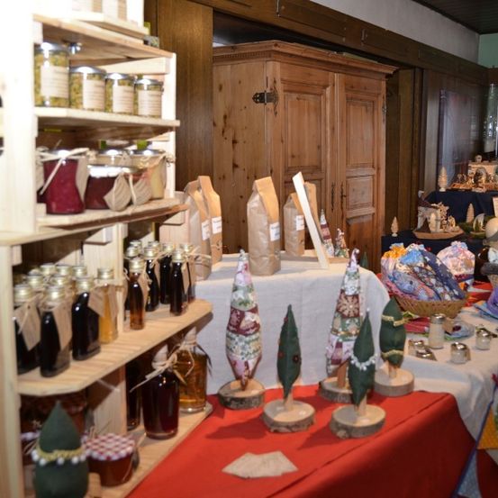 Ein Raum mit Holzregalen, die verschiedene Gläser, Flaschen und Körbe präsentieren. Dekorationen und kleine Bäume schmücken die Tische, zusammen mit einem Holzschrank und gerahmten Kunstwerken.