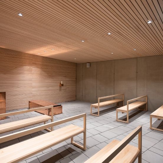 Ein leerer Raum mit Holzbänken, gefliesten Böden und einer Holzwand. Eine kleine Holzbox steht in der Ecke. Die Decke hat Lichter und eine Kerze.