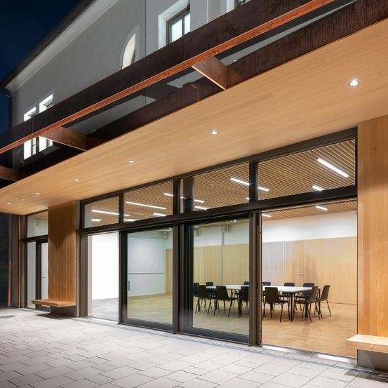 Das Innere eines modernen Gebäudes mit großen Glasfenstern und einem Konferenzraum im Inneren, beleuchtet von Lichtern in der Nacht.