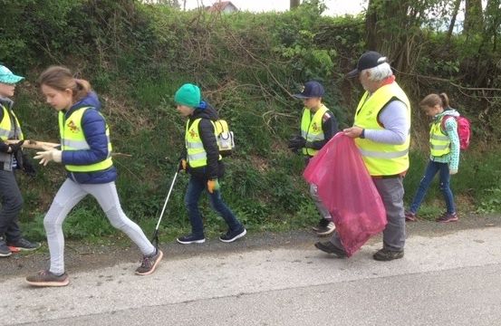 Eine Gruppe von Personen, darunter Kinder und ein Erwachsener, reinigt einen Straßenrand und hält Mülltüten in der Hand.