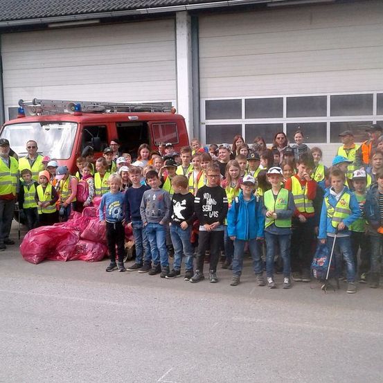 Eine Gruppe von Kindern und Erwachsenen in gelben Westen posiert für ein Foto vor einem Gebäude und einem roten Feuerwehrwagen.