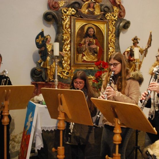 Eine Gruppe von Musikern spielt Blasinstrumente in einer Kirche, mit einem Gemälde von Jesus dahinter.
