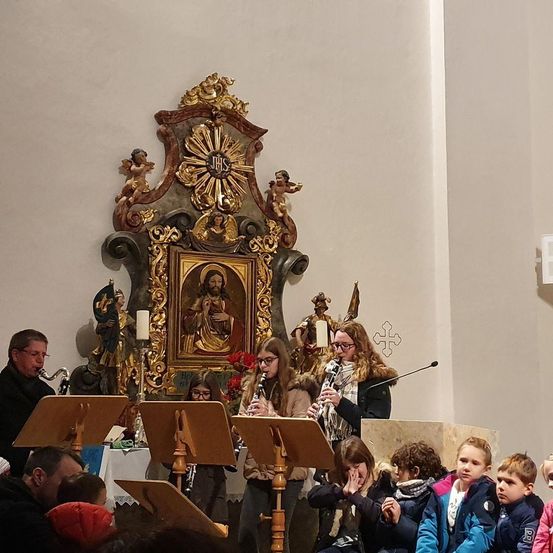 Ein musikalischer Auftritt in einer Kirche, bei dem Musiker Instrumente spielen und einige Kinder aufmerksam in der vorderen Reihe zuhören.
