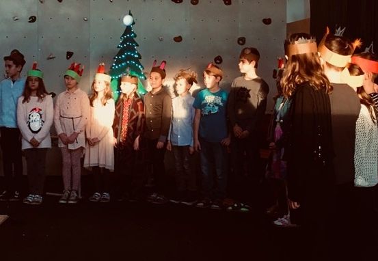 Eine Gruppe von Kindern, die Kopfbänder mit Weihnachtsbäumen und Sternen tragen, steht in einer Reihe auf einer Bühne.