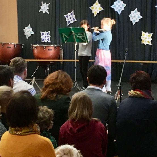 Zwei Mädchen spielen Flöten auf der Bühne mit einem Hintergrund aus Schneeflocken, Trommeln und einem zuschauenden Publikum.