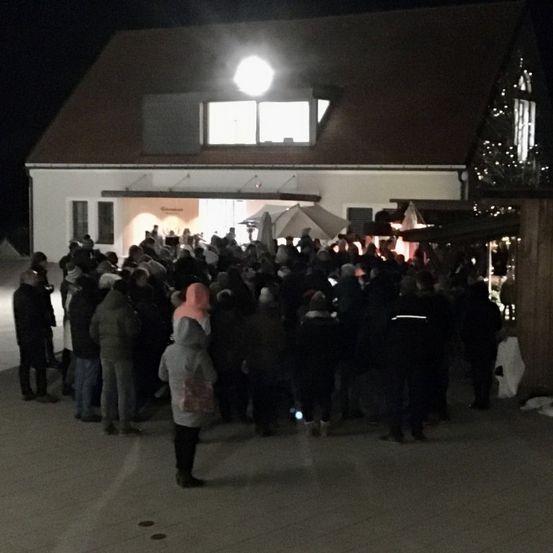 Eine große Menschenmenge versammelt sich bei Nacht vor einem Gebäude. Viele Leute tragen Winterkleidung. Ein helles Licht erhellt den Eingang.