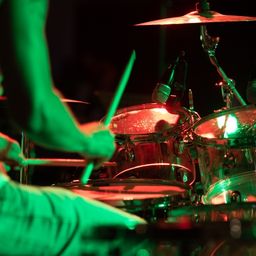 Ein Schlagzeuger spielt einen Satz mit beleuchteten Trommeln und Becken unter einem grünen Scheinwerferlicht.