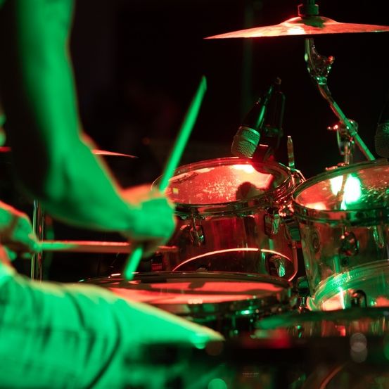 Ein Schlagzeuger spielt einen Satz mit beleuchteten Trommeln und Becken unter einem grünen Scheinwerferlicht.