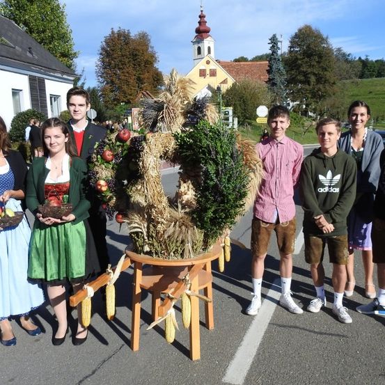 Eine Gruppe von Menschen steht um eine dekorative Anzeige von Früchten und Pflanzen vor einer Kirche.