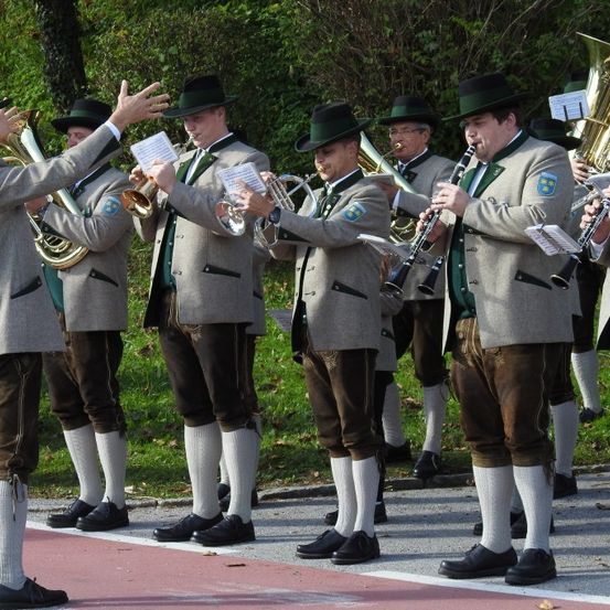 Eine Gruppe von Musikern in traditioneller Kleidung spielt verschiedene Instrumente, darunter Trompeten, Posaunen und Klarinetten, auf einer Straße stehend.