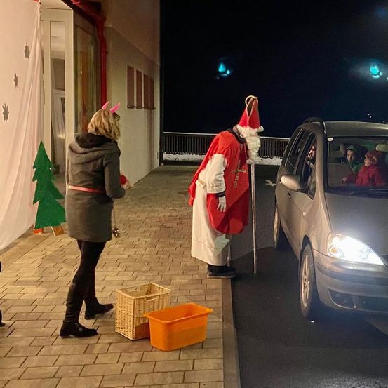 Eine Frau steht auf einem Bürgersteig, während ein Mann in Santa Claus-Kostüm zu ihr spricht. Hinter ihm ist ein Auto auf der Straße geparkt.