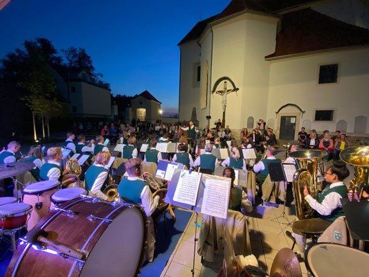 Eine Band spielt bei Nacht auf einer Bühne im Freien, mit Zuschauern vor einer Kirche.