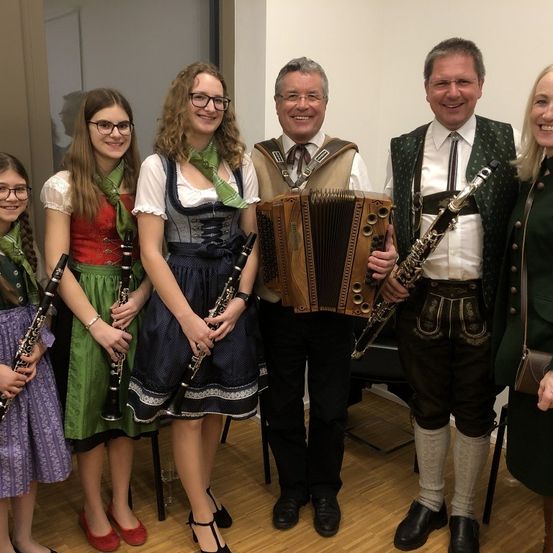 Fünf Personen posieren für ein Foto, während sie Musikinstrumente wie Klarinetten und ein Akkordeon halten. Sie sind alle in traditioneller Kleidung gekleidet.