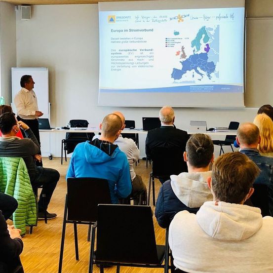 Ein Mann hält eine Präsentation auf einer Leinwand über Europa im Stromverbund vor einer Gruppe von Menschen, die in Stühlen sitzen.