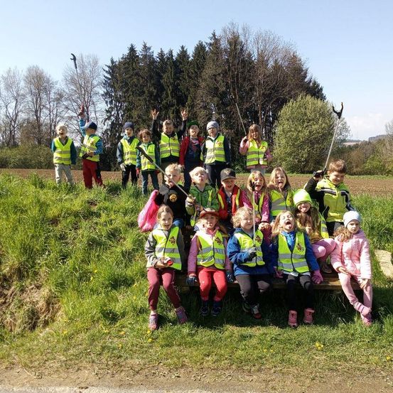 Eine Gruppe von Kindern in Warnwesten posiert für ein Foto auf einem Grashügel mit Bäumen im Hintergrund.