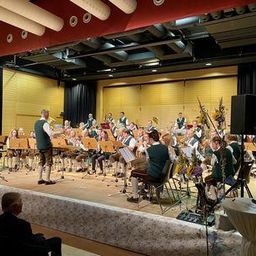 Eine Band spielt auf der Bühne, mit Musikern, die verschiedene Instrumente spielen, während ein Publikum zuschaut.